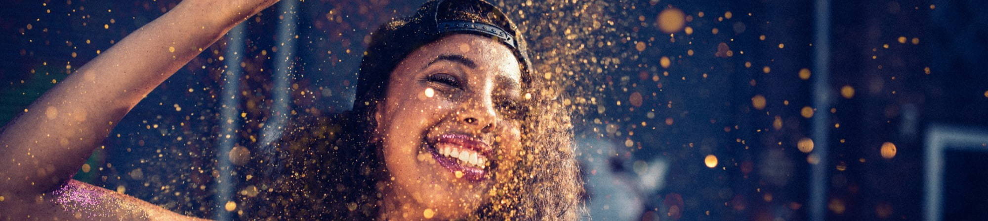 Smiling Woman wearing backwards baseball cap throwing gold glitter in the air