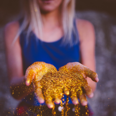 Blonde woman in a royal blue tank top with gold glitter pouring out of her hands